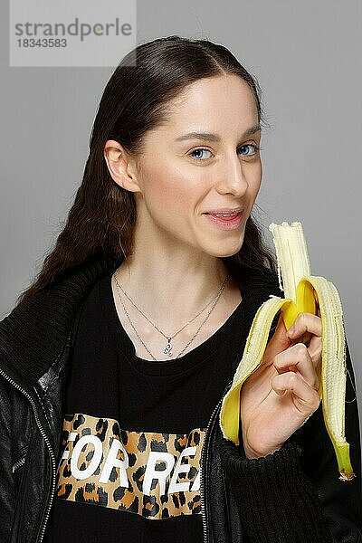 Hübsches Mädchen in Lederjacke beißt frische Banane. sauberes natürliches Make-up  lange Haare  blaue Augen