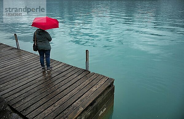 Ältere Frau  Best-Ager  mit rotem Regenschirm  schlechtes Wetter  Seepromenade am Brienzersee  Brienz  Kanton Bern  Berner Oberland  Schweiz  Europa