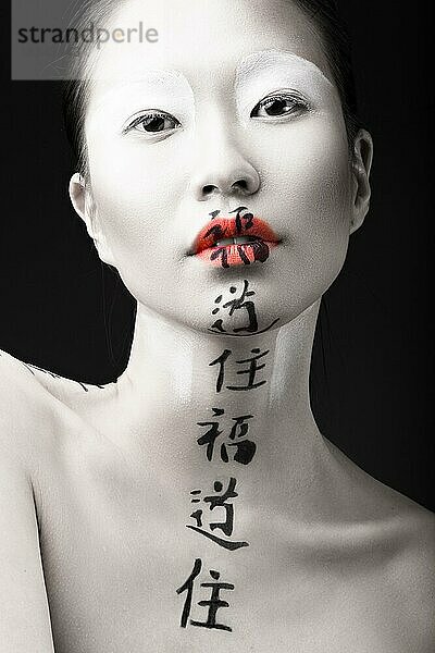 Schönes asiatisches Mädchen mit weißer Haut  roten Lippen und Hieroglyphen im Gesicht. Art Beauty Bild. Bild im Studio auf einem schwarzen Hintergrund aufgenommen