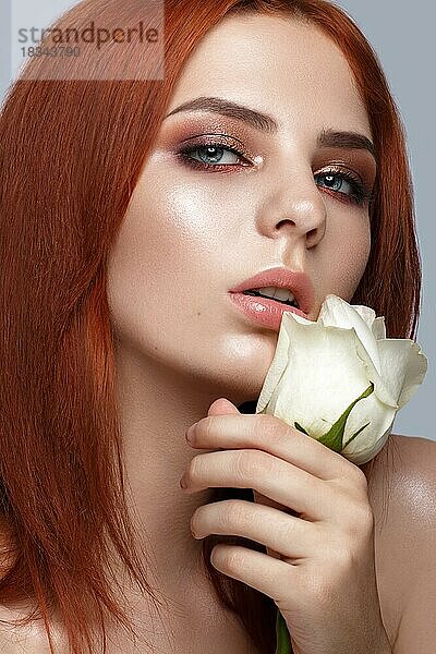 Schönes rothaariges Mädchen mit klassischem Make-up und Rose in den Händen. Schönes Gesicht. Foto im Studio aufgenommen