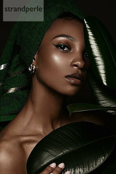 Schöne schwarze Frau mit einem grünen Handtuch auf dem Kopf und klassischem Make-up. Schönes Gesicht. Foto im Studio aufgenommen