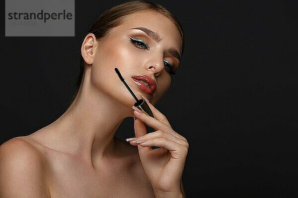 Schönes Mädchen mit sexy Lippen und klassischen Make-up mit kosmetischen Mascara Pinsel in der Hand. Schönes Gesicht. Foto im Studio aufgenommen