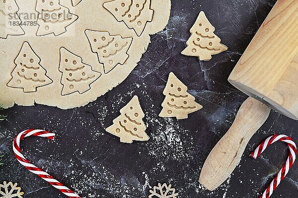 Overhead-Flachlegekonzept zum Backen von Weihnachtsplätzchen mit ausgerolltem Plätzchenteig  Plätzchen in Form von Weihnachtsbäumen  Nudelholz und Zuckerstangen