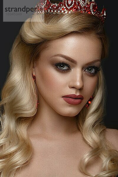 Schönes blondes Mädchen mit einer goldenen Krone und Ohrringen und professionellem Abend-Make-up. Schönes Gesicht. Bild im Studio aufgenommen