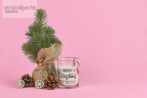 Weihnachtsbaum in Jutesack mit Tannenzapfen  Kerze mit der Aufschrift Frohe Weihnachten und Schneeflocken-Ornament auf rosa Hintergrund mit Kopierraum