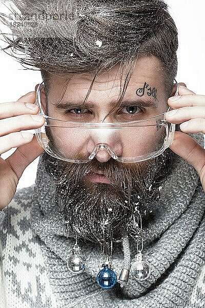 Lustiger bärtiger Mann in einem Neujahrsbild mit Schnee und Dekorationen auf seinem Bart. Fest der Weihnacht. Fotos im Studio aufgenommen