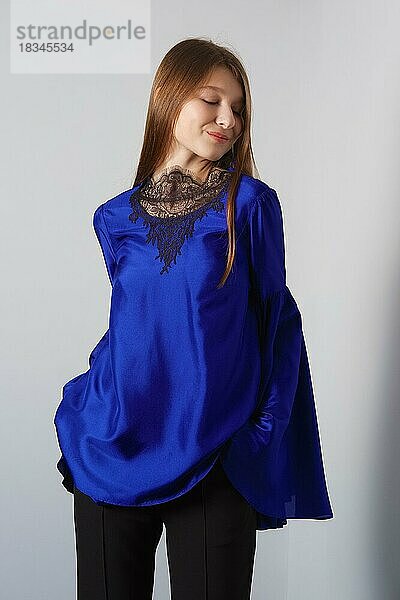 Attraktive Mode-Modell in blauer Seide Bluse mit Schmetterling Ärmel posiert für Lookbook in der Nähe von grauen Wand