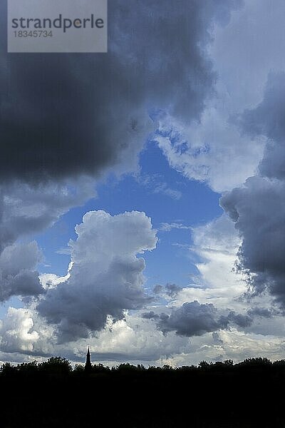 Lücke in weißen und grauen Wolken (Kumuluswolken) mit blauem Himmel an einem Regentag im Sommer