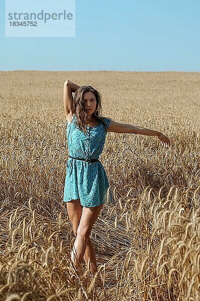 Unbeschwertes Mädchen im blauen Sommerkleid steht unter der Sonne in einem Weizenfeld