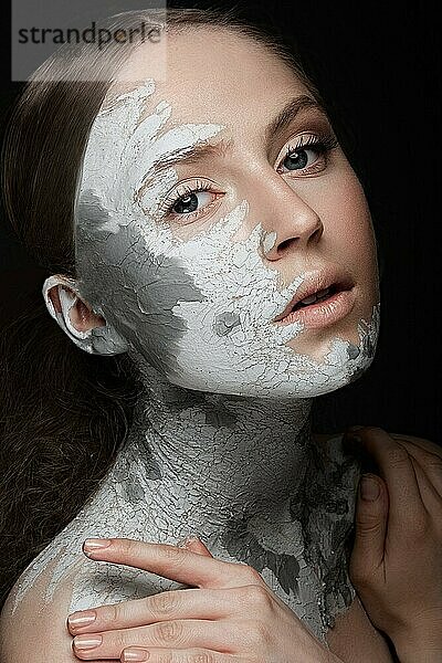 Schönes Mädchen mit Schlamm im Gesicht. Kosmetische Maske. Schönheit Gesicht. Bild im Studio auf einem schwarzen Hintergrund genommen