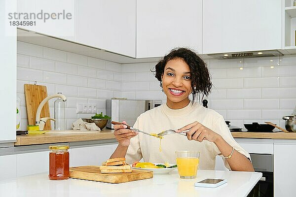 Lächelnde afrikanisch-amerikanische Frau beim traditionellen Frühstück mit Spiegelei und frischem Gemüse zu Hause