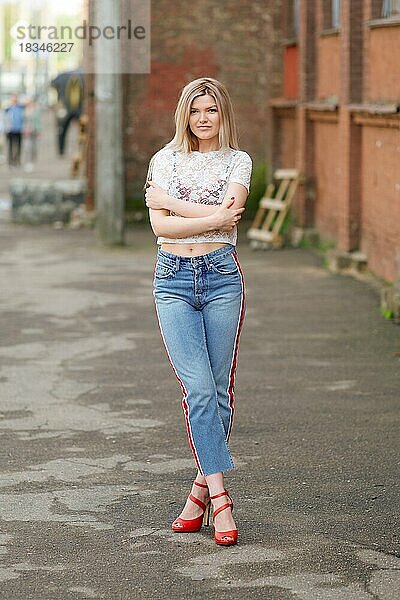 Attraktives blondes Mädchen in kurzen Jeans  Spitzenbluse und roten Schuhen posiert auf der Straße