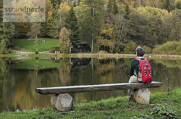 Ältere Frau mit Rucksack  Best Ager  sitzt einsam auf Holzbank  Ebnisee  Kaisersbach  Herbst  Schwäbischer Wald  Baden-Württemberg  Deutschland  Europa