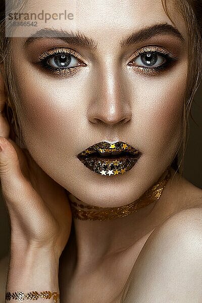 Schönes Mädchen mit einem goldenen glänzenden Make-up und Sternen auf ihren Lippen. Schönes Gesicht. Foto im Studio aufgenommen