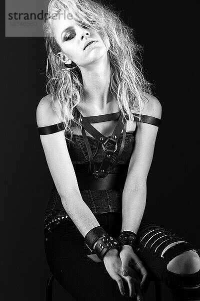 Gewagtes Mädchenmodell in schwarzem Lederkleid im Rock-Stil  dunkles Make-up  nasse Haare und Armbänder an den Armen. Das Bild wurde im Studio aufgenommen. Schwarz-Weiß-Bild