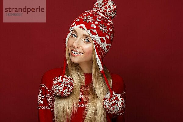 Schönes blondes Mädchen in einem Neujahrsbild in warmer Mütze und Pullover. Schönes Gesicht mit festlichem Make-up. Foto im Studio aufgenommen