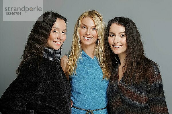 Drei attraktive Mädchen in Wollmänteln posieren im Studio. Glücklich lächelnde Freundinnen. Natürliches Make-up