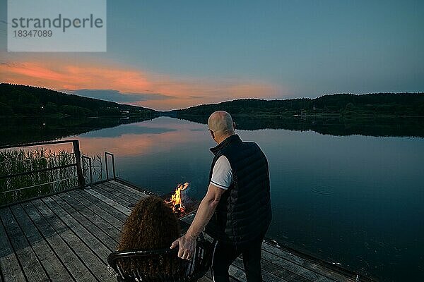 Niedliches Paar beobachtet den Sonnenuntergang am Feuer sitzend auf dem Pier  Rückansicht