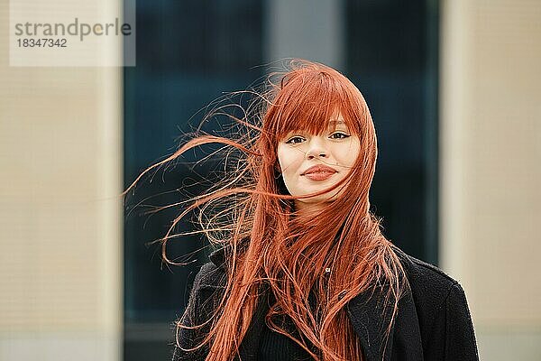 Straßenporträt einer glücklichen jungen rothaarigen Frau an einem windigen Tag