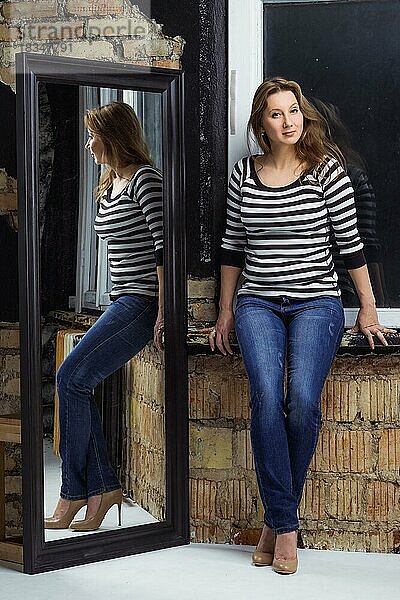Größe plus Modell in Bluse und Jeans posiert im Studio in der Nähe des Spiegels