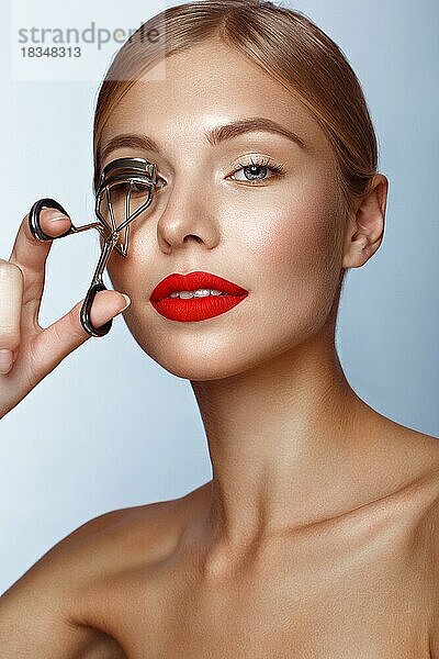Schönes Mädchen mit roten Lippen und klassischem Make-up mit Lockenwickler in der Hand. Schönes Gesicht. Foto im Studio aufgenommen