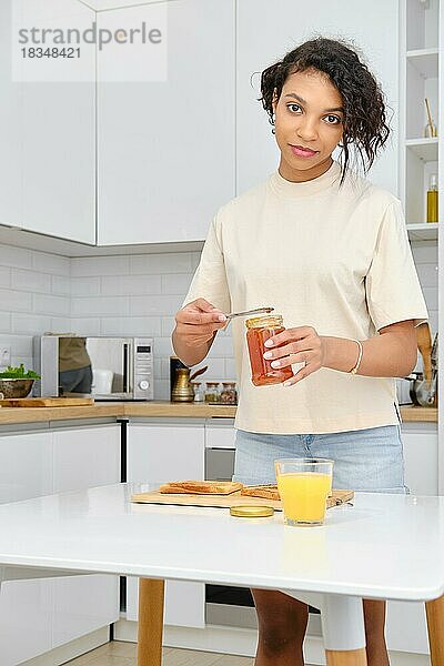 Eine afroamerikanische Frau hält Aprikosenmarmelade in der Hand. Sie wird einen süßen Toast machen