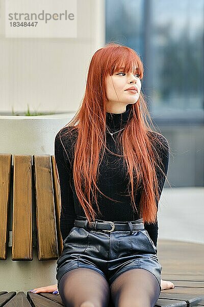 Junge rothaarige Frau sitzt geduldig auf einer Bank und schaut weg