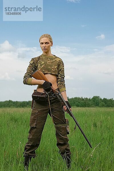 Attraktives Jägermädchen mit doppelläufigem Jagdgewehr steht in der Mitte des Feldes