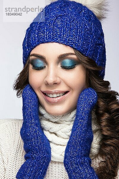 Schönes Mädchen mit sanftem Make-up  Locken und einem Lächeln in winterlicher blauer Strickmütze. Warmes Winterbild. Schönes Gesicht. Bild im Studio aufgenommen