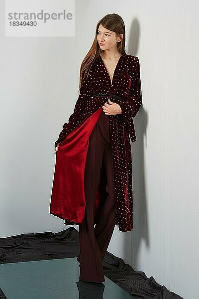 Attraktive Mode-Modell in Hosen und lange Robe posiert für Lookbook in der Nähe von grauen Wand