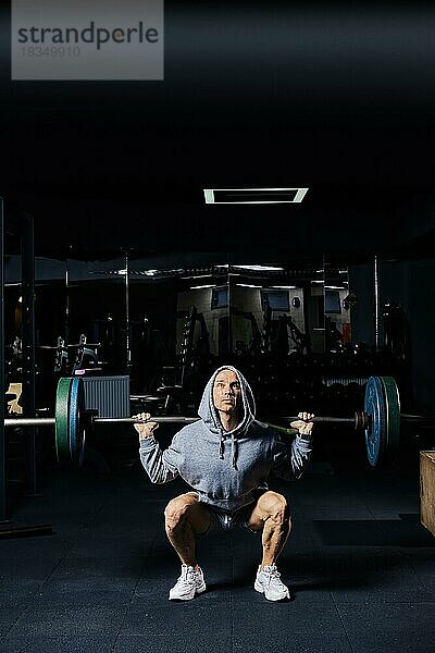 Low-Key-Foto eines muskulösen Mannes  der Kniebeugen mit einer Langhantel im Fitnessstudio trainiert