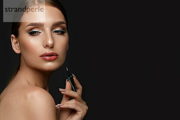 Schönes Mädchen mit sexy Lippen und klassischen Make-up mit kosmetischen blauen Eyeliner in der Hand. Schönes Gesicht. Foto im Studio aufgenommen