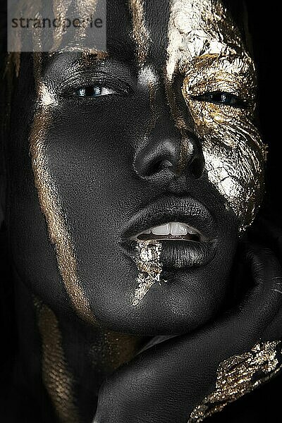Modeporträt eines dunkelhäutigen Mädchens mit goldenem Make-up. Bild im Studio auf einem schwarzen Hintergrund genommen