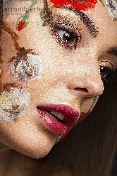 Schönes brünettes Mädchen mit Locken und einem Blumenmuster im Gesicht. Schönheit Blumen. Porträtaufnahme im Studio