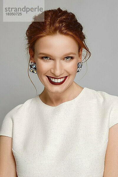 Lächelndes Modemodell mit roten  matten Lippen und Edelsteinohrringen. Perfekte Haut  natürliches Make-up