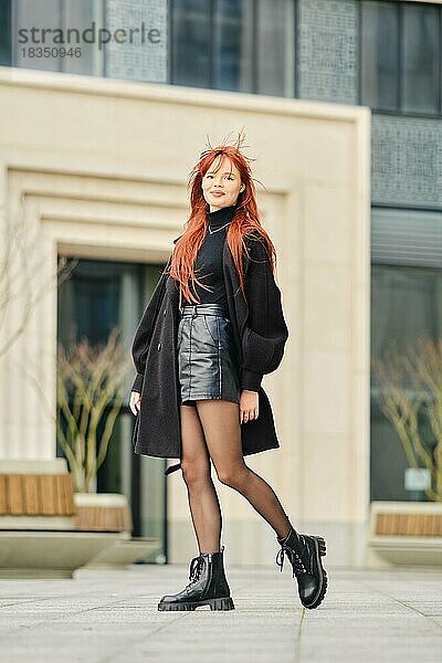 Junge stilvolle Frau mit roten Haaren geht die Straße entlang