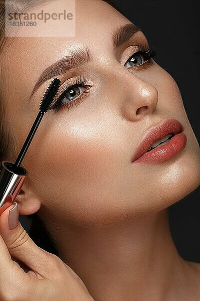 Schönes Mädchen mit sexy Lippen und klassischen Make-up mit kosmetischen Mascara Pinsel in der Hand. Schönes Gesicht. Foto im Studio aufgenommen