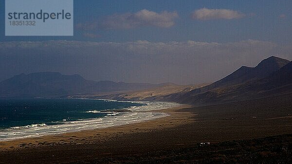 Leuchtturm  Wilder Süden  Westküste  Bergkette  Wellen  starke Brandung  karge Landschaft  blauer Himmel  wenige Wolken  Fuerteventura  Kanarische Inseln  Spanien  Europa
