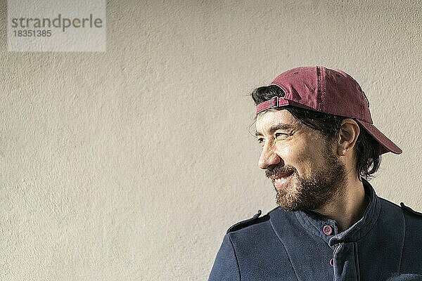 Nahaufnahme eines lateinischen Mannes im Profil  der an einer Mauer in einem Park lächelt