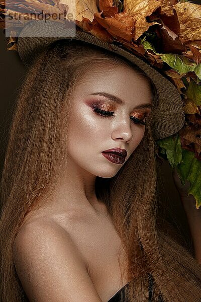 Schöne blonde Modell Herbst Hut mit Locken  hellen Make-up und roten Lippen. Die Schönheit des Gesichts. Porträtaufnahme im Studio auf einem braunen Hintergrund