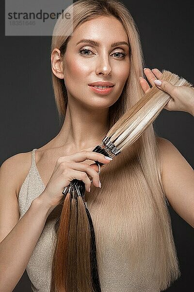 Schönes blondes Mädchen mit einem perfekt glatten Haar  klassisches Make-up mit einer Palette für Haarverlängerungen in den Händen. Schönes Gesicht. Bild im Studio aufgenommen