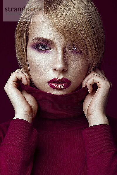 Schöne blonde Frau in einem roten Pullover mit hellem Make-up und dunklen Lippen. Schönes Gesicht. Bild im Studio aufgenommen