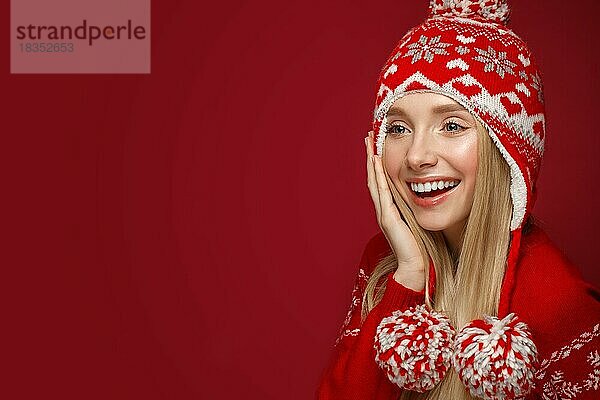 Schönes blondes Mädchen in einem Neujahrsbild in warmer Mütze und Pullover. Schönes Gesicht mit festlichem Make-up. Foto im Studio aufgenommen