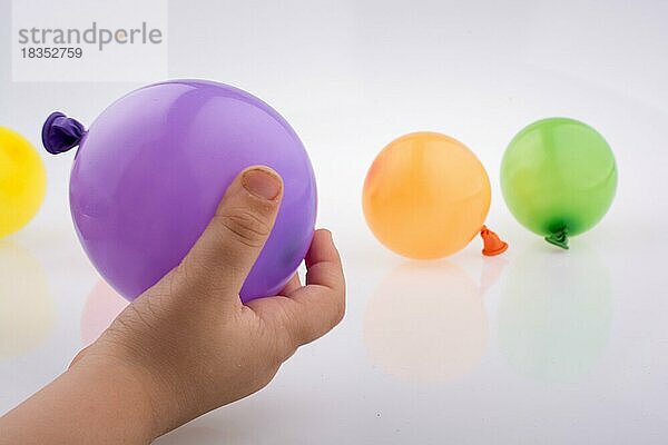 Hand hält einen bunten kleinen Ballon mit bunten Luftballons auf dem weißen Hintergrund