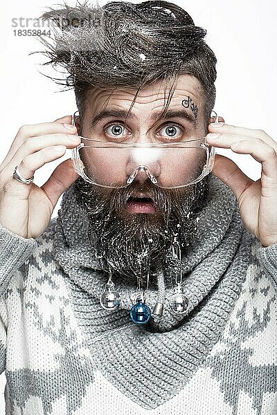 Lustiger bärtiger Mann in einem Neujahrsbild mit Schnee und Dekorationen auf seinem Bart. Fest der Weihnacht. Fotos im Studio aufgenommen