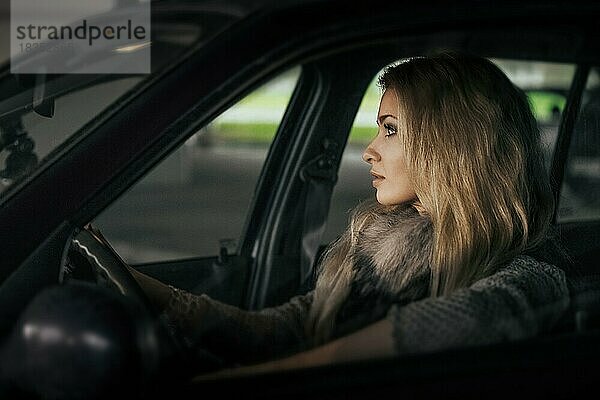 Stadtporträt einer hübschen blonden Fahrerin im Auto. Nachtszene. Dame hinter dem Steuer. Weichzeichner Foto  enthalten ein wenig Lärm