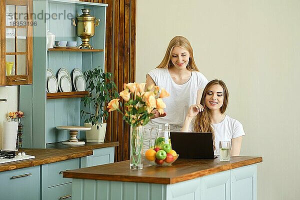 Zwei fröhliche junge Frauen führen einen Online-Videogespräch auf einem Laptop  winken mit den Händen und lachen