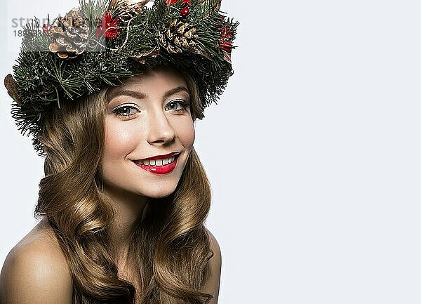Schönes Mädchen mit einem Kranz aus Weihnachtsbaumzweigen und -zapfen. Neujahrsbild. Schönheit Gesicht. Bild im Studio auf einem weißen Hintergrund genommen