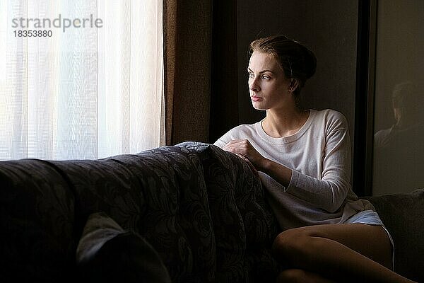 Hübsches Mädchen sticht zu Hause auf dem Sofa und schaut zum Fenster