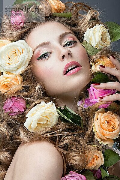 Schönes Mädchen mit vielen Blumen im Haar und leuchtend rosa Make-up. Frühling Bild. Schönheit Gesicht. Bild im Studio auf einem grauen Hintergrund aufgenommen